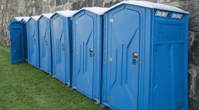 Row of blue portable toilets lined up on grass against a stone wall for event sanitation in Salt Lake City, UT